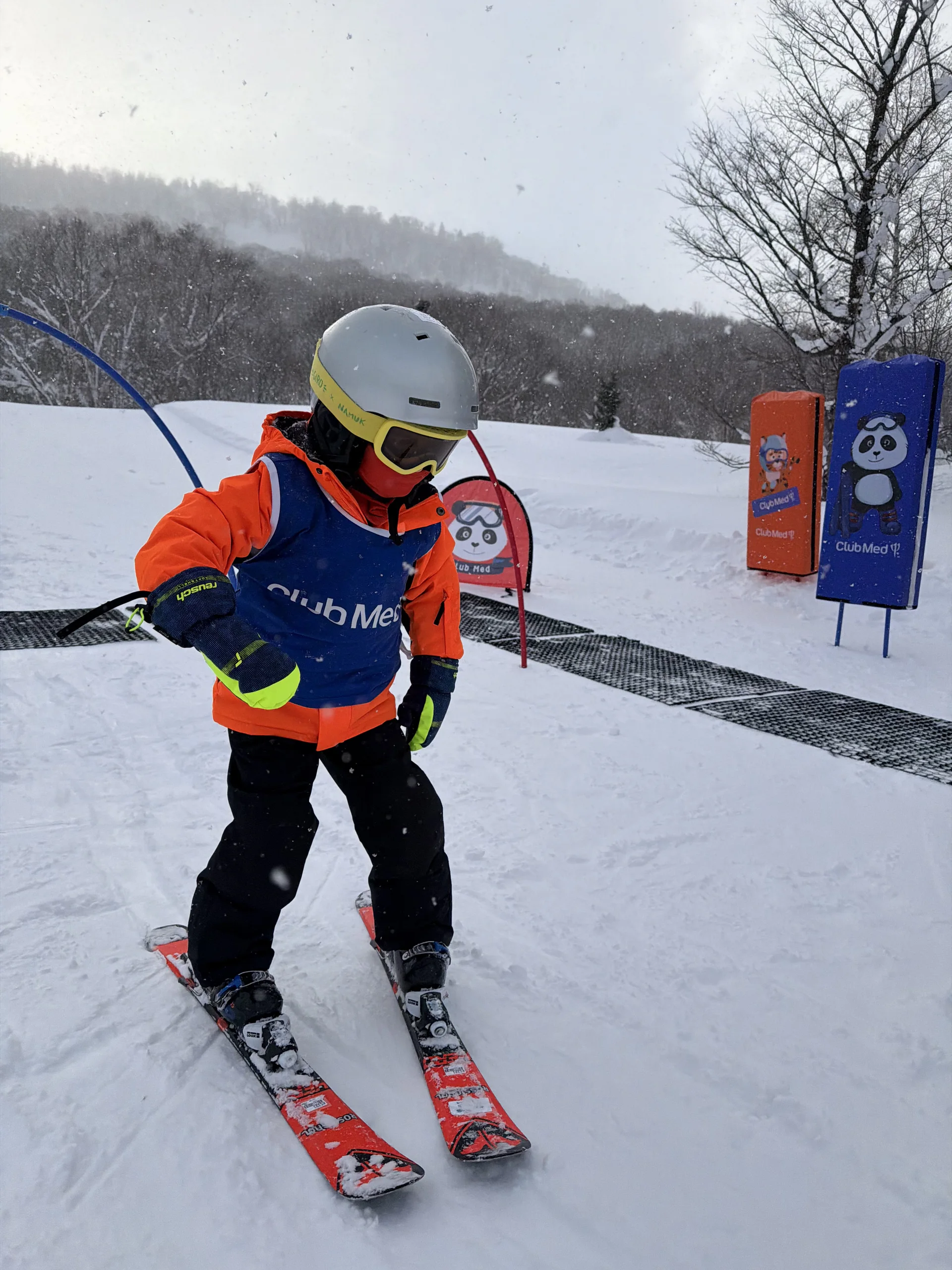 A young child in a Club Med ski-school bib learning to ski on a gentle run in Hokkaido.