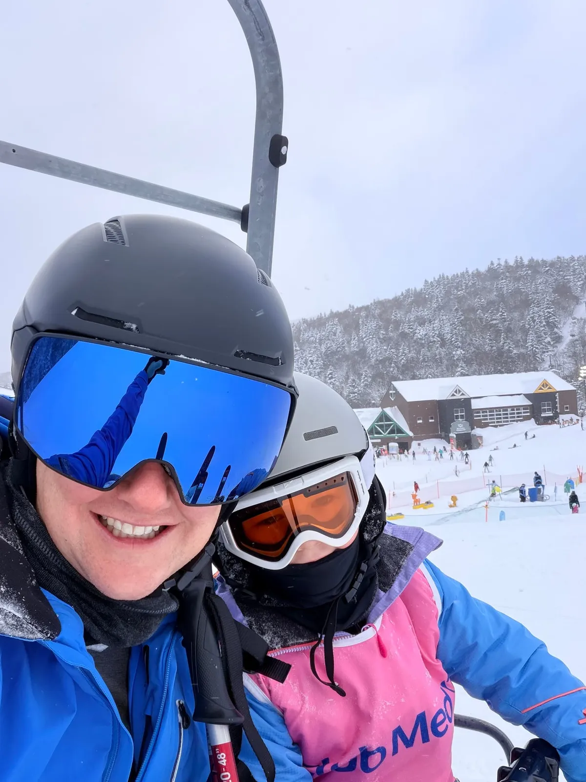 A parent and child ride a chairlift together at a snowy Japanese ski resort.