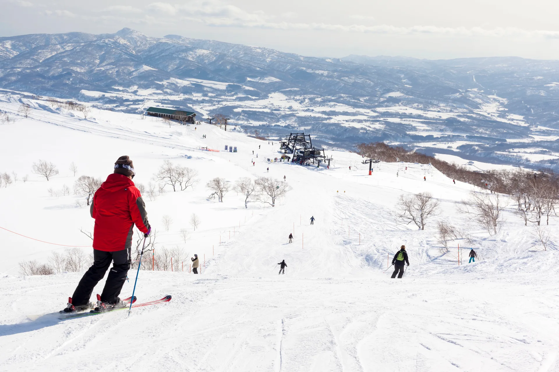A skier at the top of a groomed run looking out over a wide, snow-covered valley at a Hokkaido ski resort.