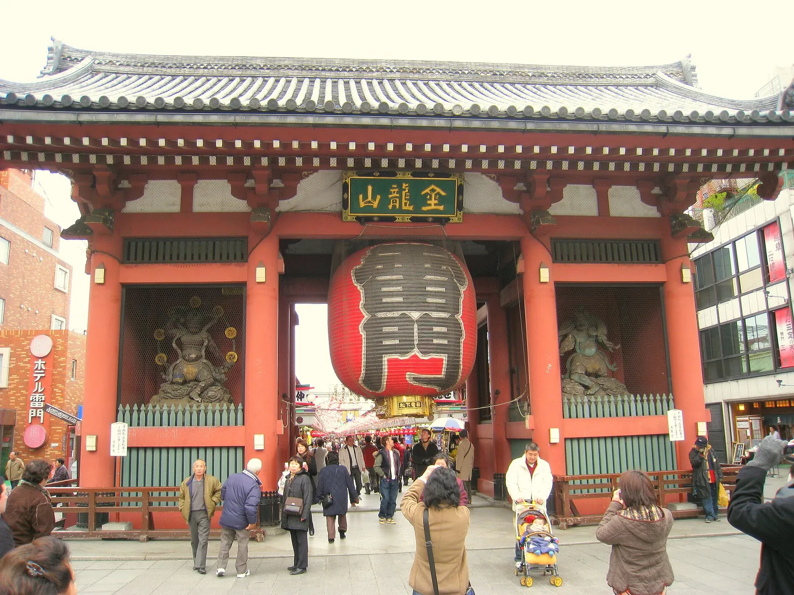 The giant red paper lantern of the Kaminarimon gate at Senso-ji temple in Asakusa, Tokyo, with visitors passing beneath.