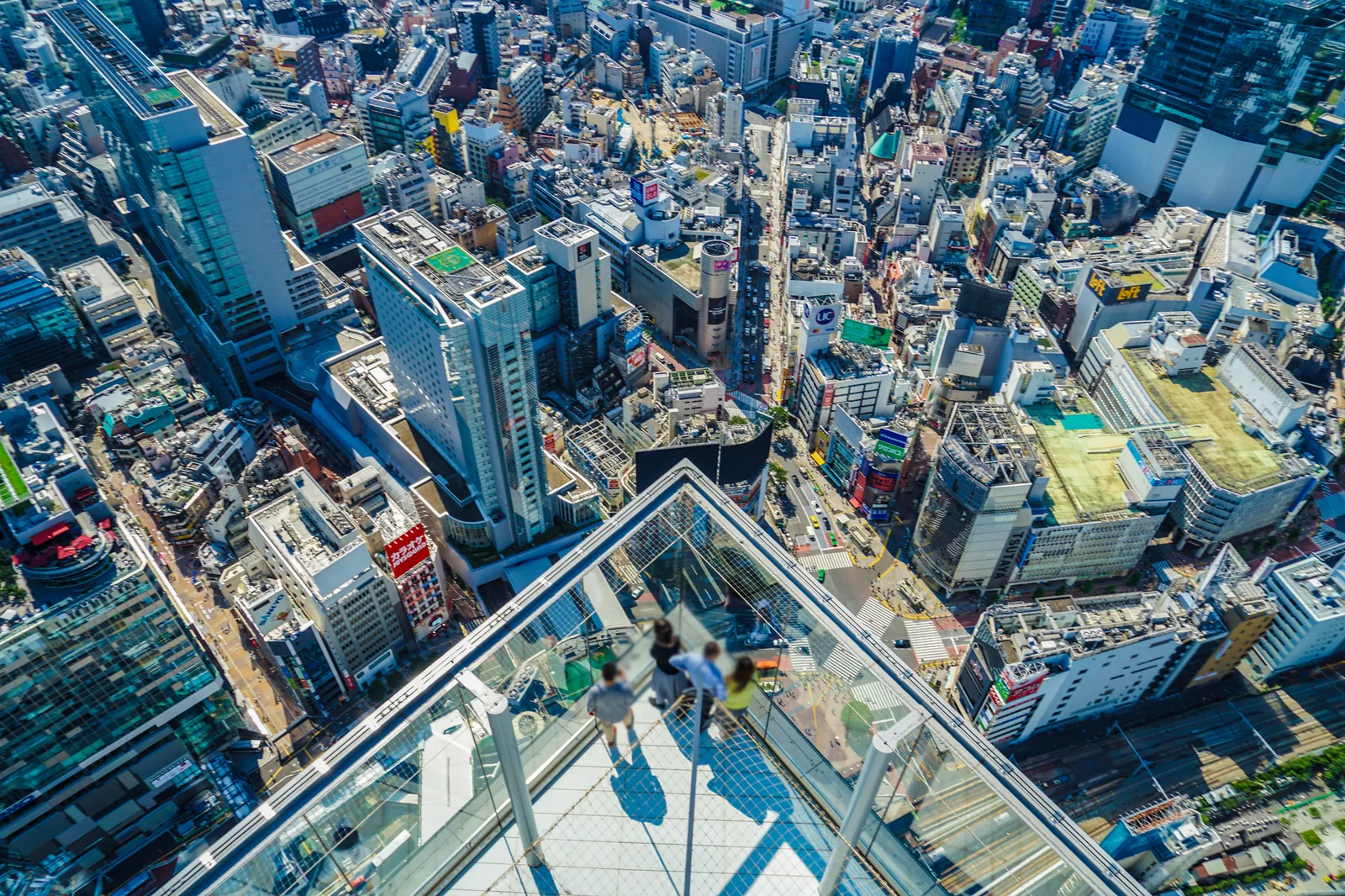 The view down over Shibuya from the open-air Shibuya Sky observation deck, with the angular glass viewpoint and the Tokyo cityscape stretching to the horizon.