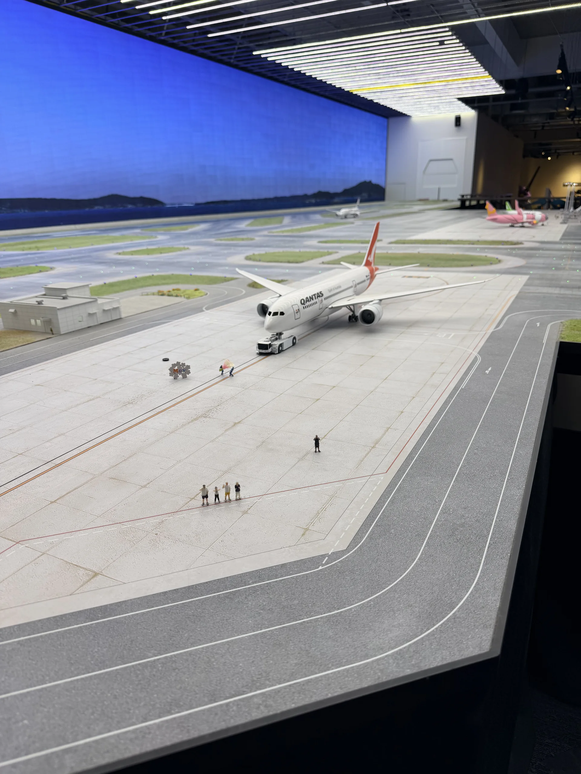 A finely-detailed miniature model of a Qantas passenger jet on the runway of the airport diorama, with tiny figures beside it, at the Small Worlds miniature museum in Tokyo.