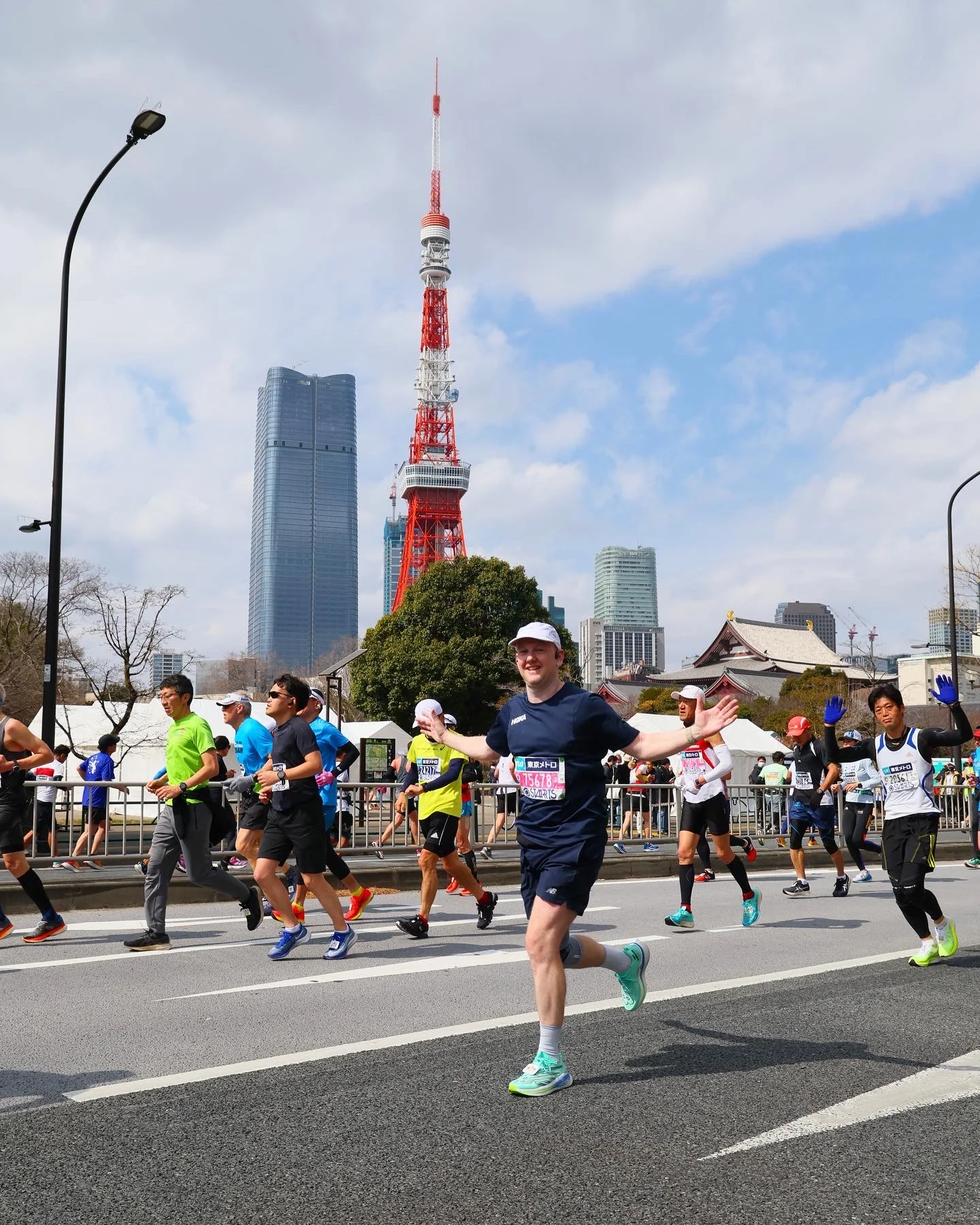 A Tokyo Marathon runner with arms outstretched passing Tokyo Tower, among a field of runners on the closed course.